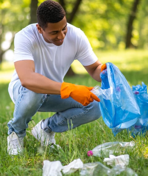Image of a man picking up trash off the ground and putting it into a blue bag