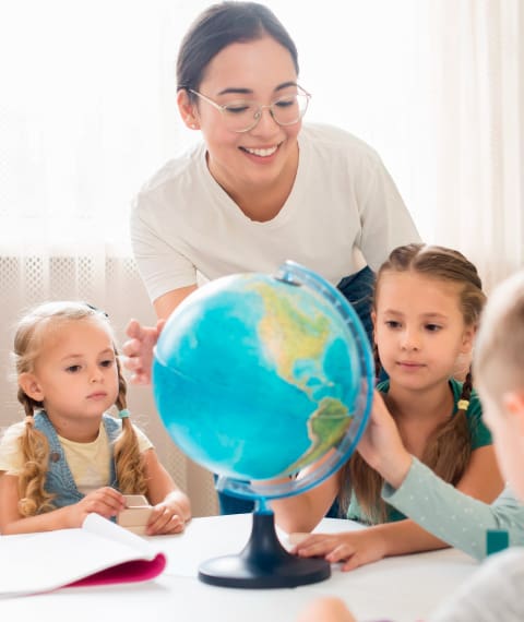 地球儀を見ている2人の女の子と教師の画像