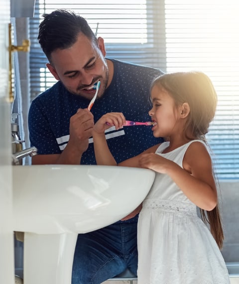 Father brushing teeth with daughter in bathroom