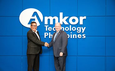 Two men shaking hands in front of Amkor logo